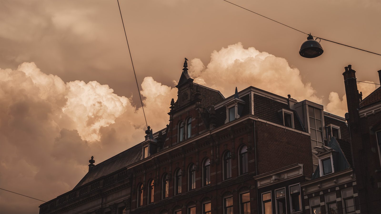 An Amsterdam façade at dusk, a hanging street lamp against amber clouds